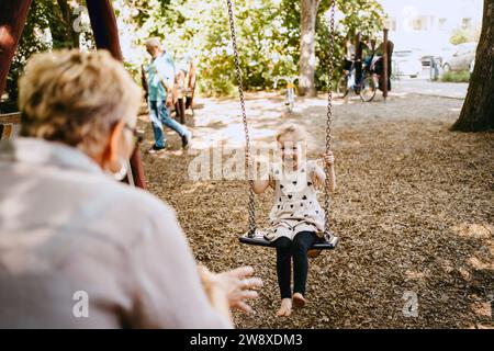 Fille joyeuse jouant sur la balançoire avec grand-mère au parc Banque D'Images