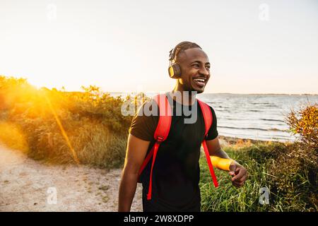 Heureux jeune homme avec sac à dos et écouteurs sans fil marchant sur le sentier Banque D'Images