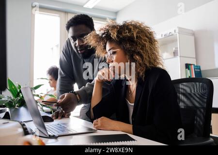Collègue masculin discutant sur ordinateur portable avec femme entrepreneur assis au bureau Banque D'Images