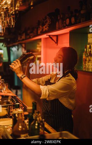 Souriante barman préparant un cocktail tout en travaillant au comptoir du bar Banque D'Images