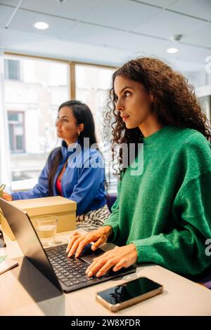 Femme d'affaires regardant loin avec ordinateur portable sur le bureau au bureau Banque D'Images
