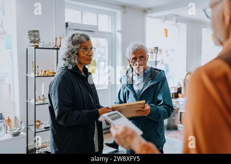 Couple senior achetant le cadre photo et parlant avec le vendeur dans le magasin d'antiquités Banque D'Images