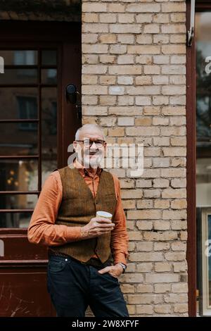 Portrait de propriétaire masculin heureux avec tasse à café debout à l'extérieur du magasin Banque D'Images