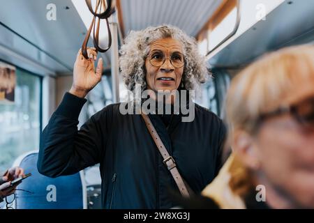 Femme âgée debout dans le bus tout en voyageant pour le travail Banque D'Images