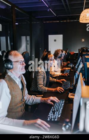 Amis seniors masculins et féminins jouant à des jeux vidéo sur des ordinateurs dans le salon de jeux Banque D'Images