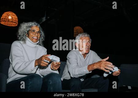 Amis seniors masculins et féminins jouant à des jeux vidéo ensemble dans le salon de jeux pendant le week-end Banque D'Images