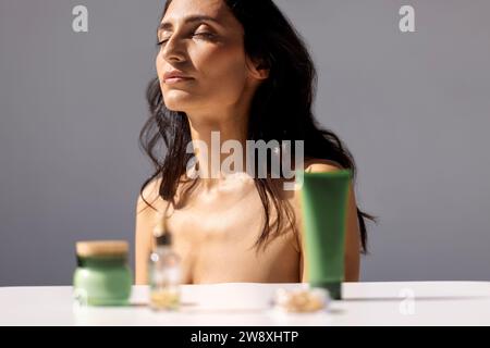 Portrait féminin rapproché d'une jeune femme attrayante avec les yeux fermés dans la lumière du soleil sur un fond gris isolé. Veillez à ce que le visage soit propre et doux Banque D'Images