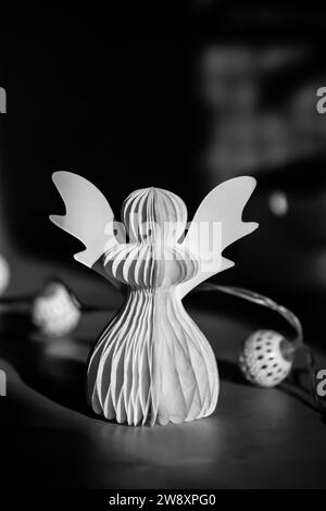 Ange de papier DIY sur un fond sombre. Symboles religieux, Noël festif, décor du nouvel an, guirlande, bougies. Photo artistique noire et blanche Banque D'Images