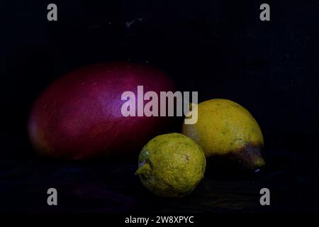 Nature morte avec mangue rouge, citrons jaunes et fond sombre Banque D'Images