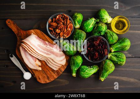 Choux de Bruxelles au bacon, noix de pécan et canneberges Ingrédients : choux de Bruxelles crus, lanières de bacon et autres ingrédients sur une table en bois Banque D'Images