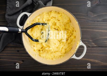 Préparation de purée de pommes de terre dans un four hollandais en fonte émaillée : écraser des pommes de terre Yukon Gold avec de l'ail rôti, du fromage mascarpone, du beurre et du lait Banque D'Images