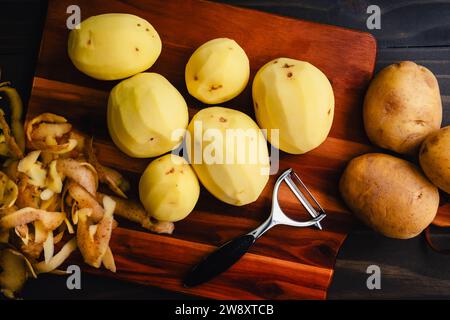 Pommes de terre Yukon Gold pelées sur une planche à découper en bois : pommes de terre jaune doré pelées et non pelées avec un éplucheur de légumes sur une table en bois Banque D'Images