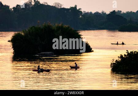 Silhouettes de personnes faisant du kayak à travers les eaux calmes du Mékong, dans l’archipel de si Phan Don, à travers des rayons de lumière dorée réfléchis par la riv Banque D'Images