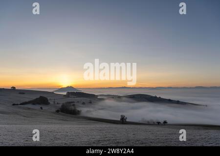 Vue de l'ancienne route de poste près de Leipferdingen dans la Hegaulandschaft hivernale et brumeuse juste devant le lever du soleil sur l'horizon du Hohenhewen Banque D'Images