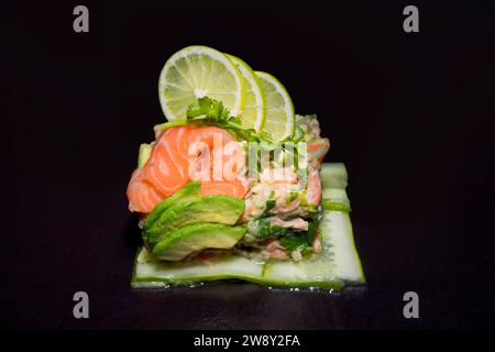 Tartare de saumon sur tranches de concombre avec coriandre fraîche, avocat et citron vert, photographie de nourriture avec fond noir Banque D'Images