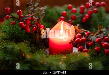 Couronne de l'Avent décorée de branches de sapin avec bougie allumée rouge sur un rebord de fenêtre en bois dans le temps avant Noël Banque D'Images