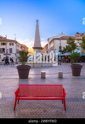 Saint Maximin, France - 1 octobre 2023 : banc rouge sur la place de Saint Maximin la Sainte Baume. Heure du coucher du soleil. Banque D'Images