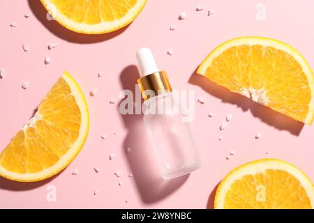 Bouteille de sérum cosmétique et tranches d'orange sur fond rose, mise à plat Banque D'Images