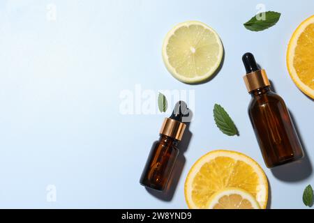 Bouteilles de sérum cosmétique, agrumes tranchés et feuilles vertes sur fond bleu clair, pose plate. Espace pour le texte Banque D'Images