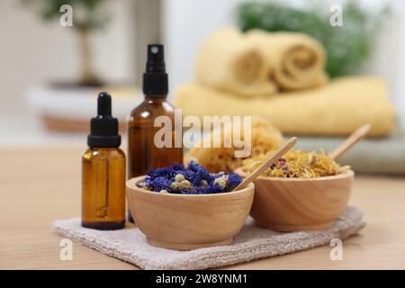 Bouteilles d'huiles essentielles, bols avec fleurs sèches et éponge naturelle sur table en bois clair, gros plan. Thérapie thermale Banque D'Images