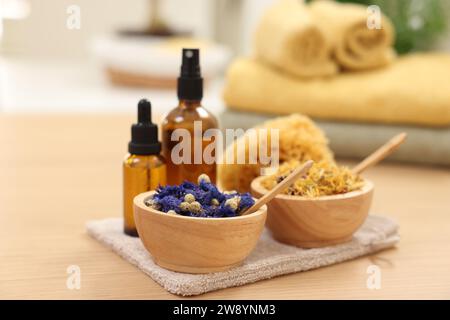 Bouteilles d'huiles essentielles, bols avec fleurs sèches et éponge naturelle sur table en bois clair, gros plan. Thérapie thermale Banque D'Images