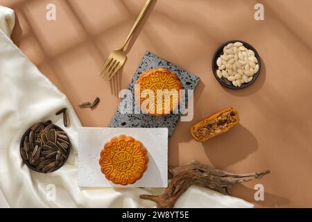 Concept de nourriture traditionnelle du Festival de la mi-automne - gâteaux de lune et types de graines décorés avec un tissu de soie blanc sur fond brun. Vue de dessus, scène pour un Banque D'Images