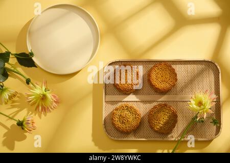 Scène pour la publicité de produit de mooncake sur fond jaune avec ombre de fenêtre. Sur le plateau en bambou, des gâteaux de lune sont exposés, décorés de fleurs et de em Banque D'Images