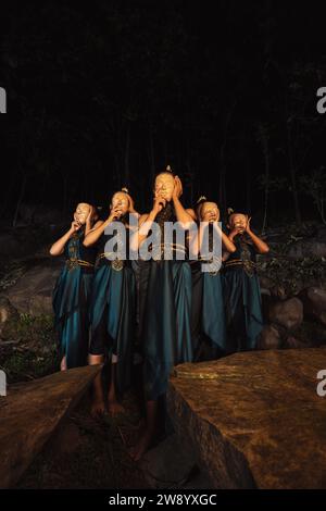 Un groupe de femmes indonésiennes tenant et portant un masque en bois brun dans une jupe verte entre la roche à l'intérieur des bois Banque D'Images