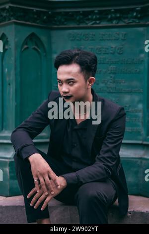 Un homme asiatique en costume noir est assis seul devant le monument funéraire avec une expression très effrayante dans l'après-midi Banque D'Images