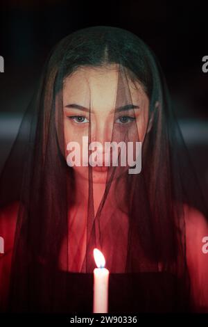 une adoratrice du diable avec un voile transparent exécute un rituel effrayant en tenant une bougie dans sa main la nuit Banque D'Images