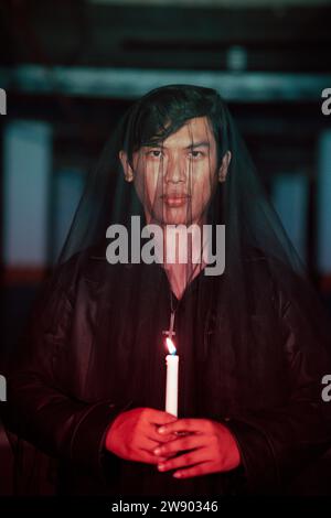 un adorateur mâle du diable avec un voile transparent exécute un rituel effrayant en tenant une bougie dans sa main la nuit Banque D'Images