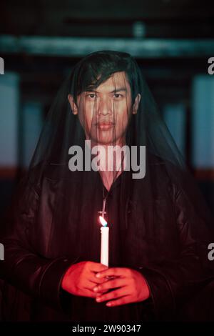 un adorateur mâle du diable avec un voile transparent exécute un rituel effrayant en tenant une bougie dans sa main la nuit Banque D'Images