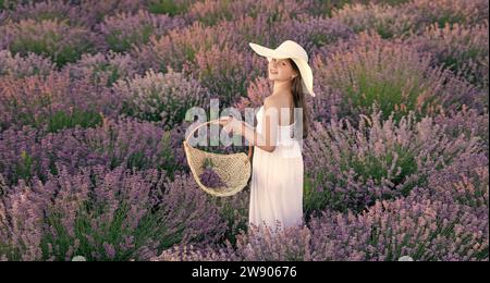 adolescente positive avec de la lavande tenant un bouquet de fleurs dans une robe marchant dans le parc de lavande Banque D'Images