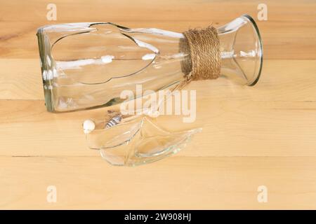 Un vase en verre cassé transparent avec des bords tranchants posé sur une table en bois Banque D'Images