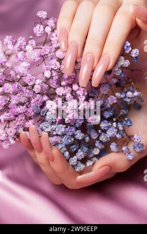 Les mains féminines avec un design de clou rose tiennent des fleurs de gypsophila. Manucure de vernis à ongles rose sur fond rose Banque D'Images