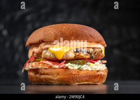 Cheeseburger de poulet, côtelette de poulet, fromage cheddar, coleslaw, coleslaw, les cornichons se rapprochent sur un fond noir. Délicieux cheeseburger. sandwich fas Banque D'Images