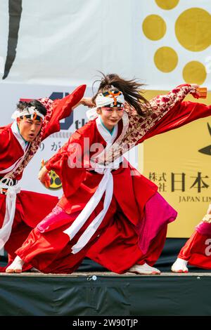 Jeune japonaise femme et homme yosakoi danseurs sur scène dansant en costume traditionnel rouge avec naruko, claqueurs, dans leurs mains. Bras tendus. Banque D'Images