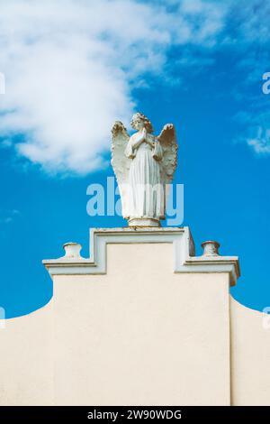 Sculpture féminine d'un ange priant sur un mur blanc avec espace de copie, avec ciel bleu avec des nuages en arrière-plan Banque D'Images