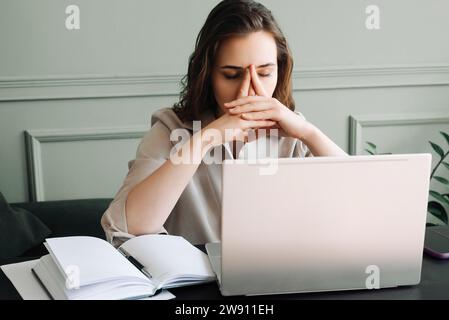 Stressé et surchargé de travail : jeune femme malheureuse avec ordinateur portable luttant contre la fatigue, la pression, la migraine et le stress. Surmenée et stressée : jeune femme avec L. Banque D'Images