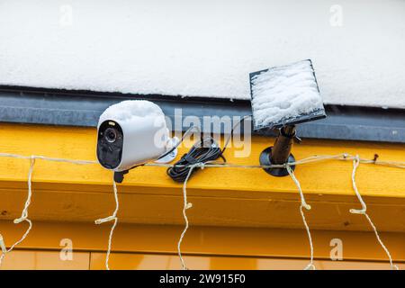 Vue rapprochée de la surveillance extérieure avec un panneau solaire enneigé sur la façade de la villa sur la journée d'hiver glaciale. Banque D'Images