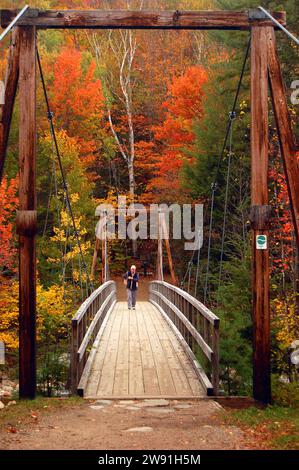 Une personne âgée active marche sur un pont suspendu piéton pour admirer les couleurs automnales des White Mountains du New Hampshire un jour d'automne en Nouvelle-Angleterre Banque D'Images