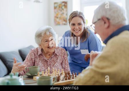 Travailleur de santé heureux avec couple senior jouant aux échecs Banque D'Images