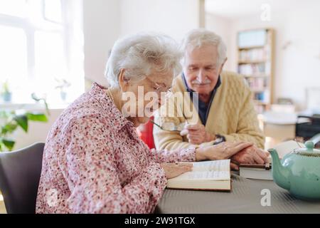 Homme âgé avec femme lisant le livre et tenant les mains à la table Banque D'Images
