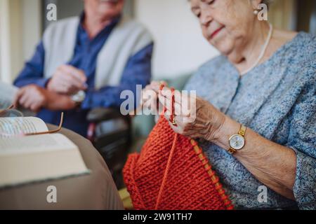 Femme senior tricotant la laine avec l'homme assis en arrière-plan Banque D'Images