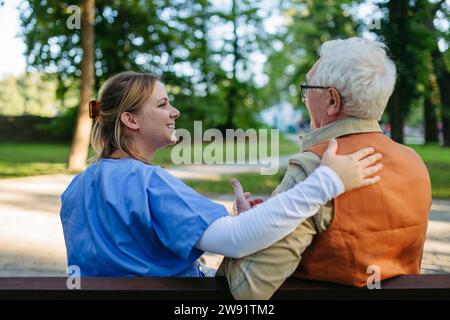 Travailleur de santé heureux soutenant et consolant homme âgé sur le banc au parc Banque D'Images