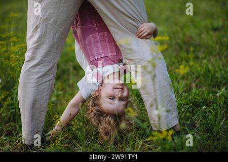 Petite fille regardant à travers les jambes de son père la tenant tête en bas Banque D'Images