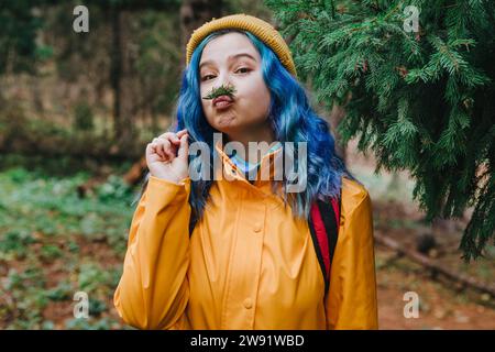 Femme portant une veste et équilibrant la brindille sur les lèvres dans la forêt Banque D'Images