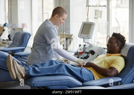 Travailleur de santé aidant le donneur à s'allonger sur le canapé au centre de don de sang Banque D'Images