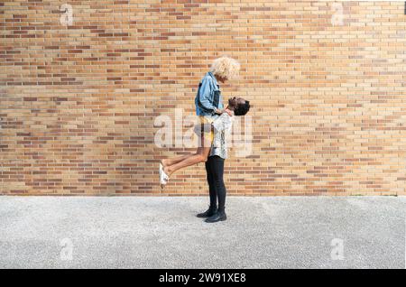 Jeune petit ami s'amusant avec une femme transgenre debout devant un mur de briques Banque D'Images