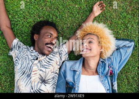 Homme heureux avec les bras levés couché à côté d'une femme transgenre sur l'herbe au parc Banque D'Images